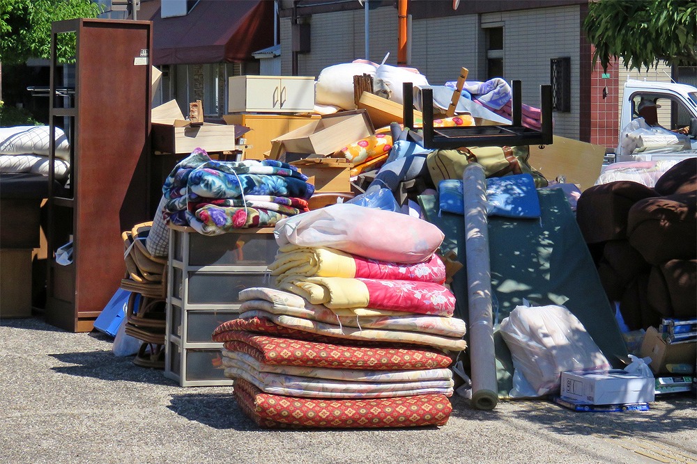 住宅前に積まれた布団、衣装ケース、タンス、椅子など多くの粗大ごみが並んでいる様子